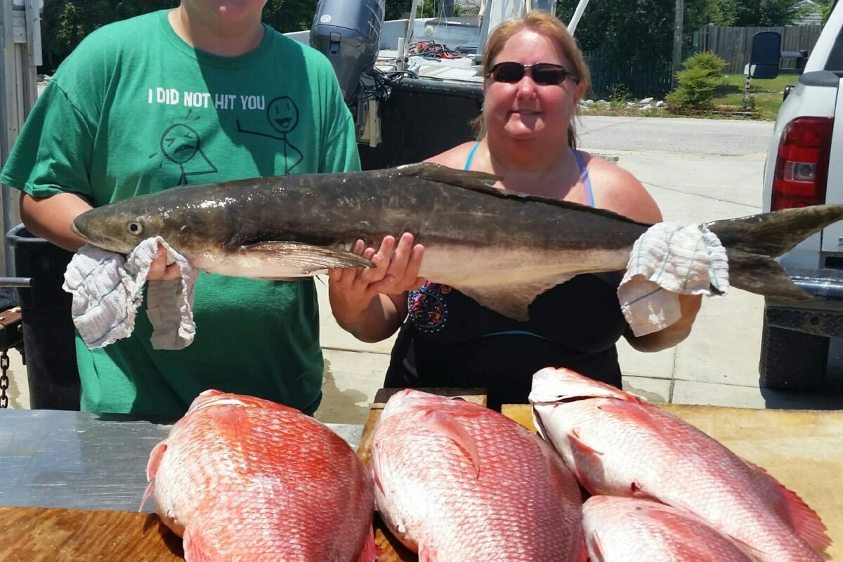 A man and a woman beaming with joy as they proudly hold a sizable fish together.