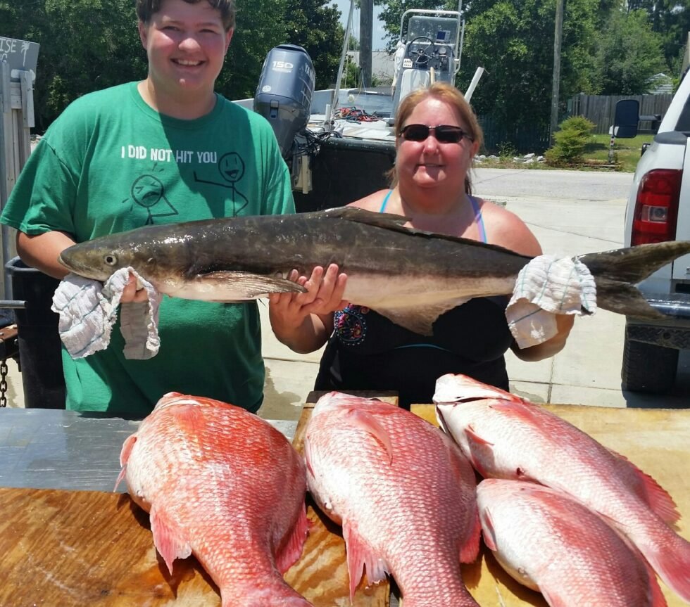 A man and a woman beaming with joy as they proudly hold a sizable fish together.