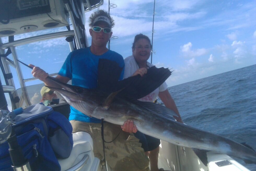The captain and a woman on a boat holding a large fish.
