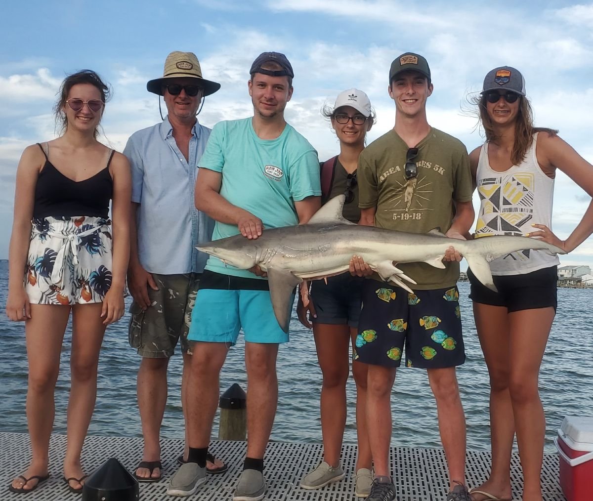 A group of anglers posing on a dock with a caught shark after a successful fishing trip in Pensacola, Florida